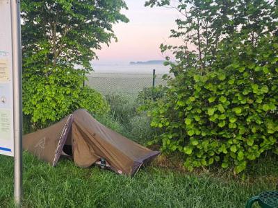 A small one man tent on a patch of grass behind an info sign. Misty fields are in the background.