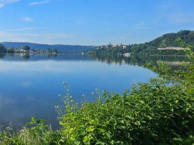 Wide calm reservoir reflecting blue sky, with wooded hills and buildings on shore.