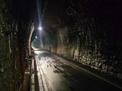 Dark stone railway tunnel converted to cycle path, lit by spaced ceiling lights.