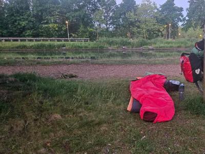 Bivy bag, bike and gear beside a canal on grassy bank at dawn.