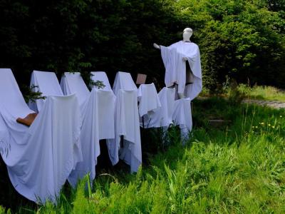 Outdoor installation of robed white mannequin figures arranged like a procession
