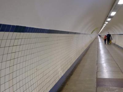 Tiled pedestrian tunnel with people walking away in the distance.