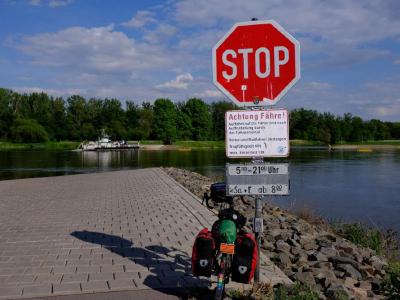 Stop sign and ferry warning above a loaded touring bike at river slipway.