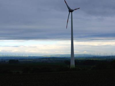  Single large wind turbine in foreground with many more on the far horizon.