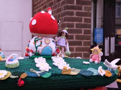Knitted fairy-tale Easter scene with toadstool house and figures on top of a red postbox.